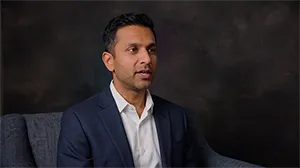 Example video shoot frame: a man in a navy blazer seated in front of a dark canvas backdrop